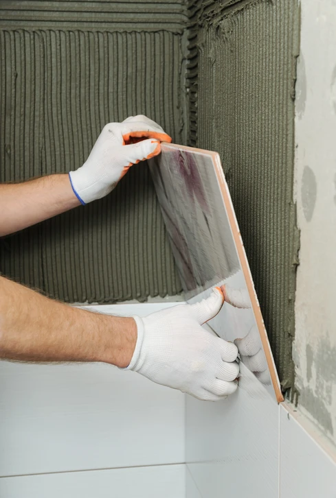 Artisan carreleur en train de poser un carreau de céramique gris marbré sur un mur